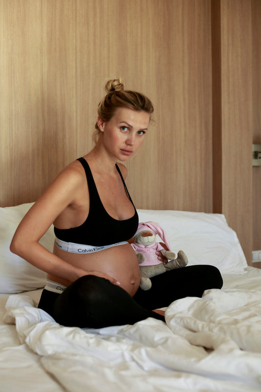 a woman in a black garment and underwear sitting on a bed